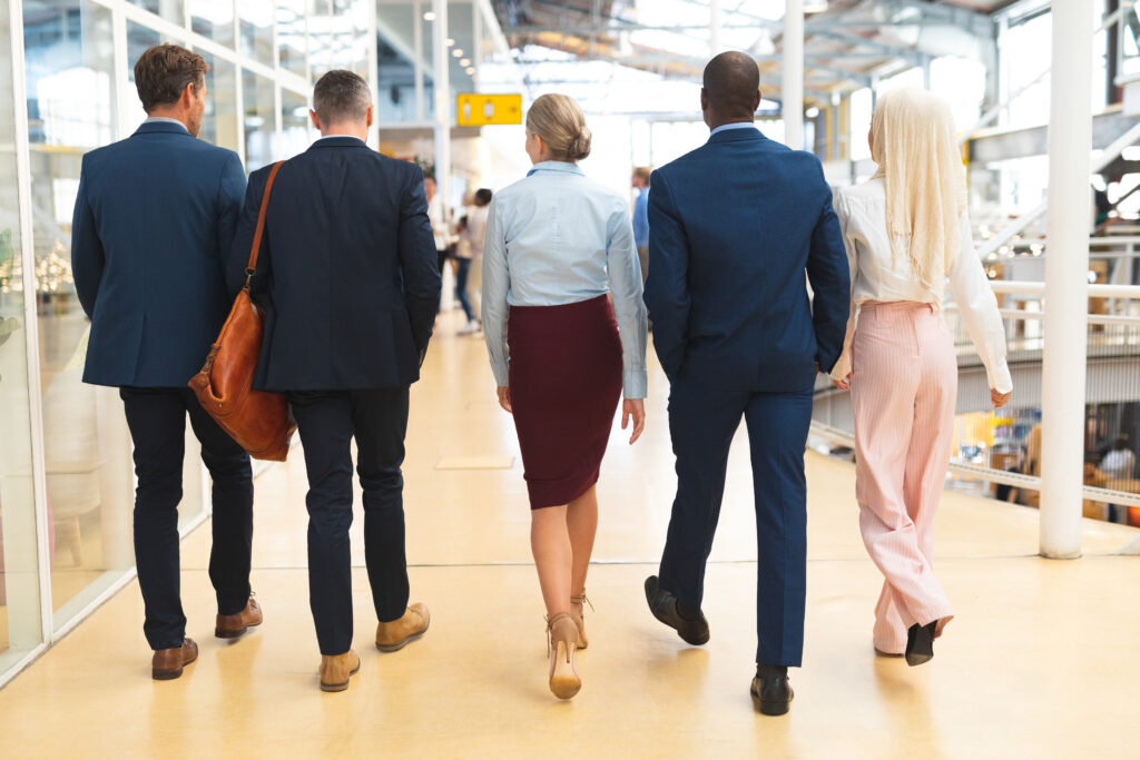 Rear view of diverse business people walking together in the corridor at office. International diverse corporate business partnership concept